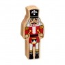 A chunky wooden red and white nutcracker toy figure in profile with a natural wood edge