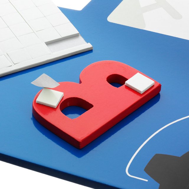 Double-sided sticky pads stuck onto a wooden letter with a peelable tab to stick to plaques