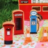 A wooden toy red postbox, red telephone box, blue fuel pump and orange cones with bus in background.