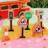 A wooden toy traffic light, stop go sign, road sign, bus stop and school sign with bus in background