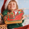 Child holding a red, gold and green Father Christmas in a sleigh toy