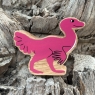 A wooden pink caudipteryx dinosaur toy figure in profile