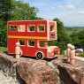 Red wooden double decker bus playset with 3 peg people sat on bricks with landscape background