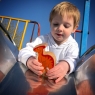 A chunky wooden toy orange parasaurolophus being played with by a toddler in the park