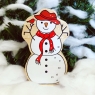 A chunky wooden white snowman toy figure in profile with a natural wood edge