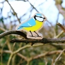 A chunky wooden blue tit toy figure in the woods on a tree branch